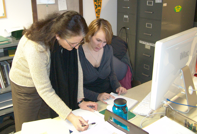 Two women read material at a desk.