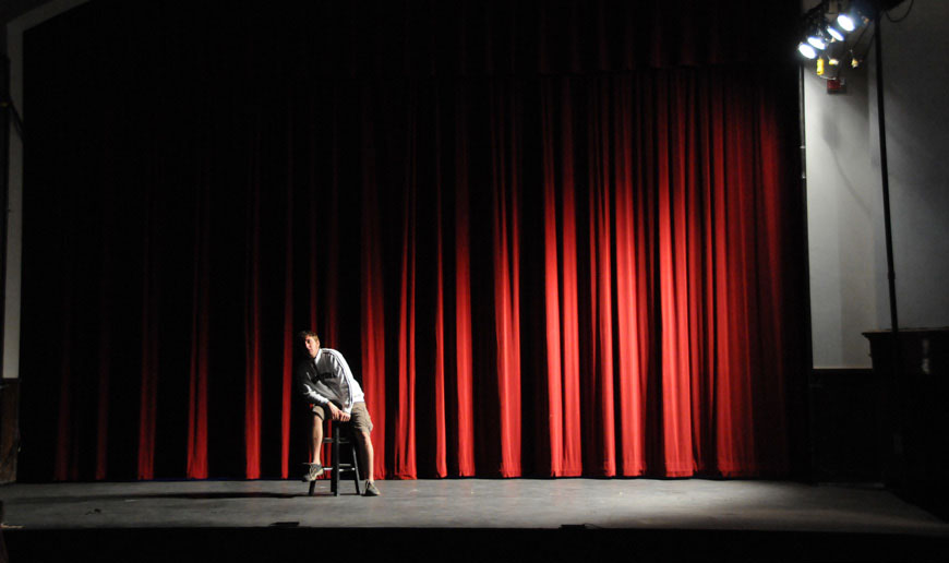 Casey Hibbert sits on a stool on a stage