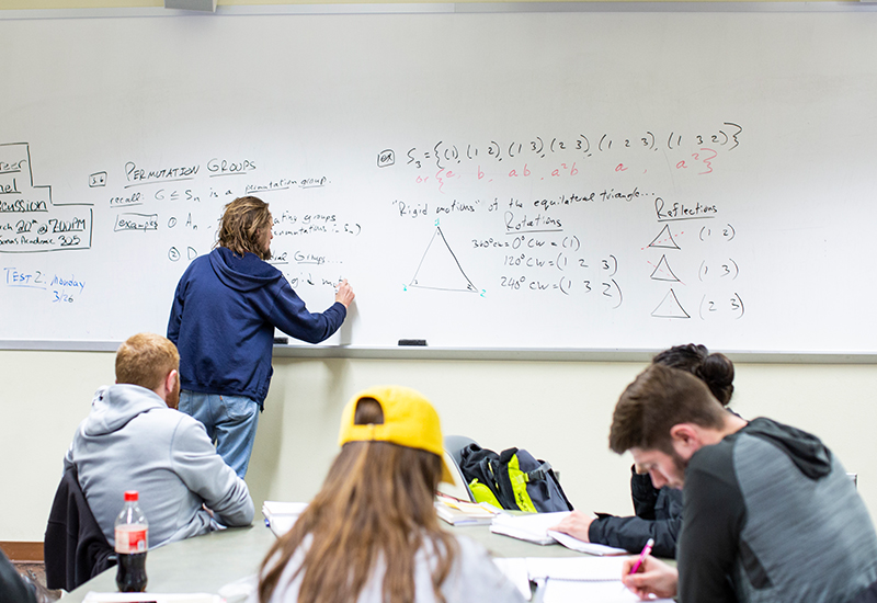 A professor writes on a whiteboard while four students take notes.