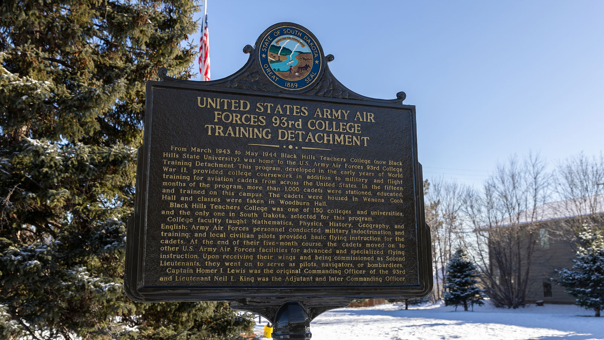 Image of Historical Marker on BHSU campus commemorating the United States Army Air Forces 93rd Bombardment Group Training Detachment at Hendricks Field in Sebring from March 1943 to May 1944, with a scenic backdrop of a snow-covered park and bare trees under a clear blue sky.