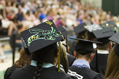 A man sits at graduation while a photo is taken of his graduation cap.