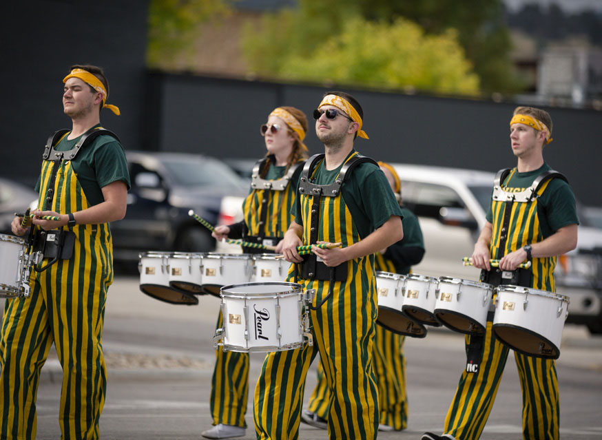 Beeline Drumline Members march down a street while playing their drums.