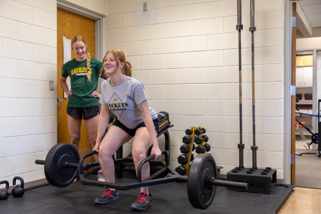 Two female Exercise Science students working with barbell equipment in the strength training facility
