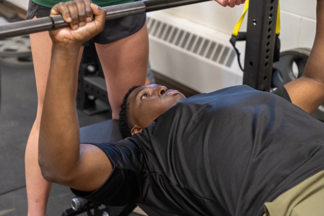 Male student performing bench press exercise with proper form during a strength training laboratory session