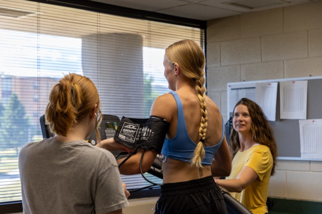 Students conducting a fitness assessment in BHSU's Exercise Science lab, with one participant on a treadmill being monitored by two classmates in a professional training environment.