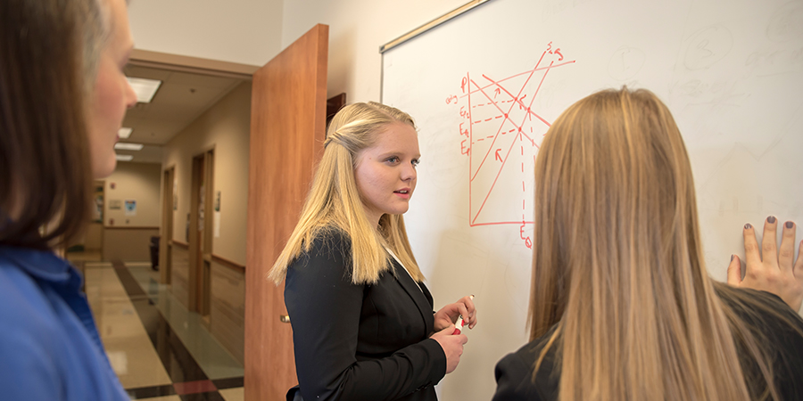 One woman writes on a whiteboard while two women observe.