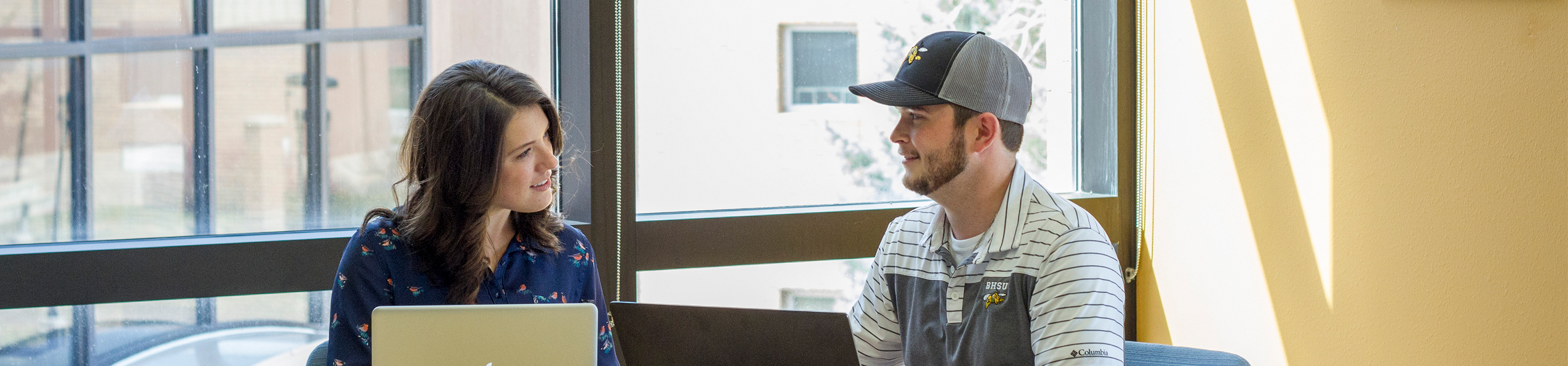 Two students working toward their strategic leadership degree sit together with laptops.
