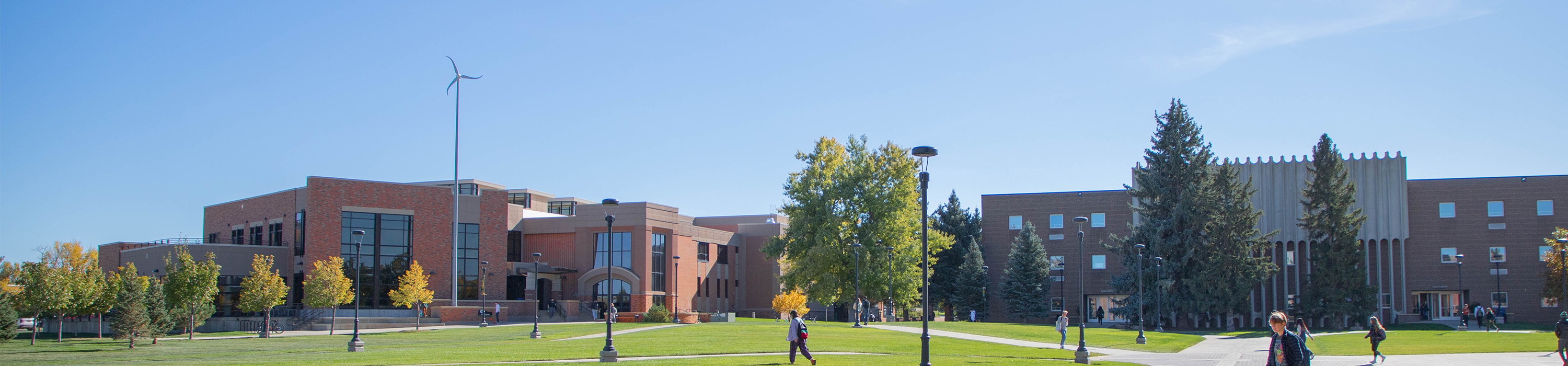The sustainability program's wind turbine overlooks the campus green while student pass in front.