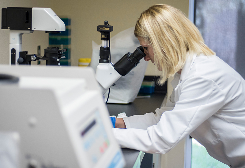 A female student looks through a microscope in a lab.