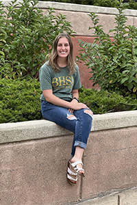 Katie Jaycox sitting on a short cement wall. 