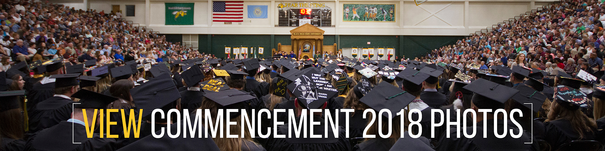 Students stand facing away from the camera with the text "View Commencement 2018 Photos" below.