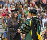 A student to the left of the image receives her degree from a man on the right.