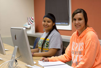 Two students sit in front of desktop computers.