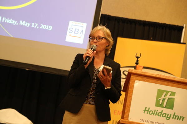 A woman speaks into a microphone while holding a phone during a business event at the Holiday Inn in Spearfish.