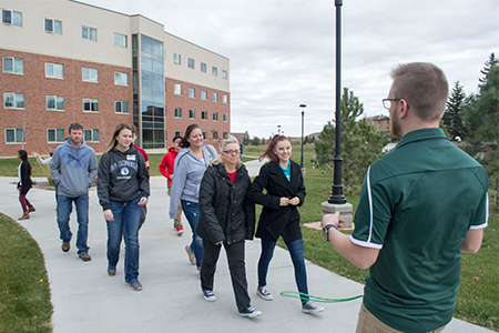 Six people are given a tour of campus by a male guide.