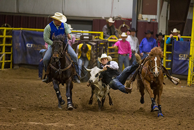 The man on the left rides a horse while the man on the right falls off his horse.