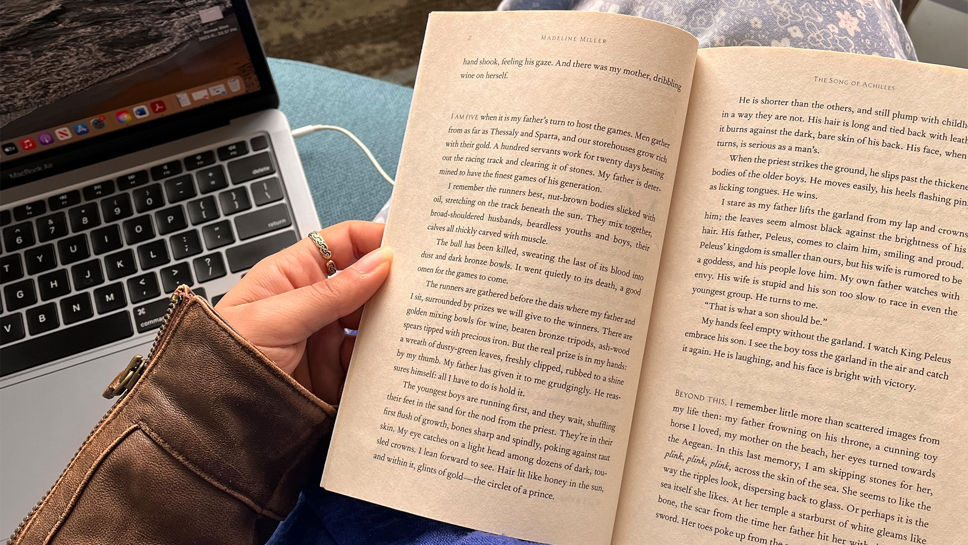 Open book, hand holding the left side of the page, computer sitting next to book