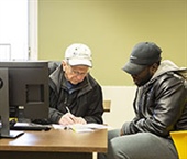 Two men sitting at a desk and filling out paperwork