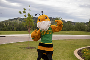 Sting mascot pointing at a face mask that they are wearing