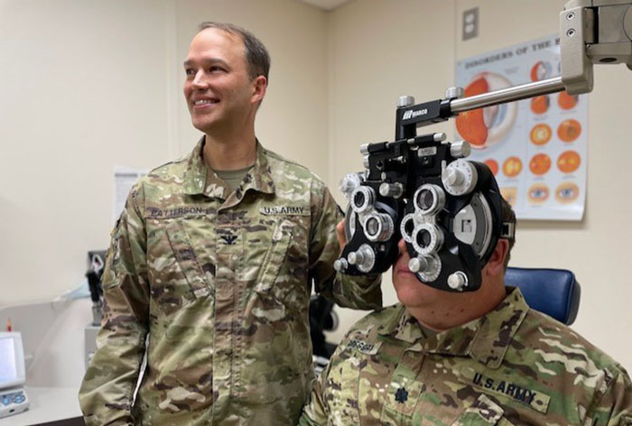 Tony Patterson in an army uniform performing an eye exam on another man in an army uniform