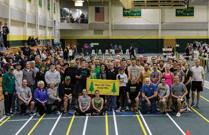 large group of BHSU alumni standing with a sign that reads "Black Hills State Alumni Mile"