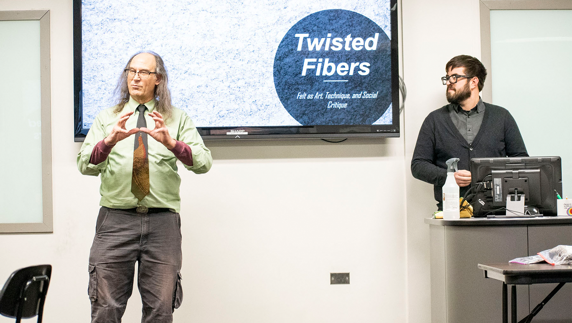 A speaker presents his lecture, titled Twisted Fibers, about felt as art.