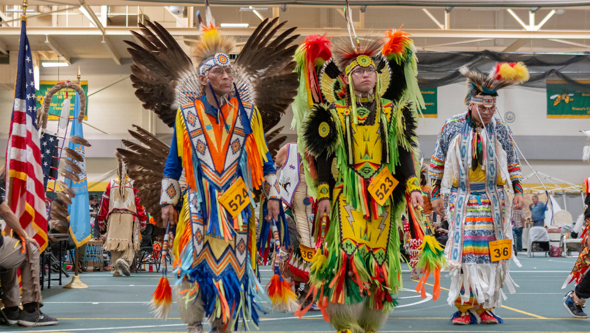 Two participants in the Wacipi stand next two each other in their traditional dress.