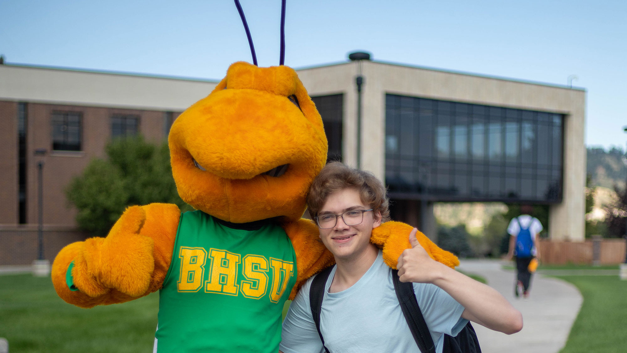 Image of BHSU mascot Sting with a student on the BHSU campus. The library building can be seen in the background.