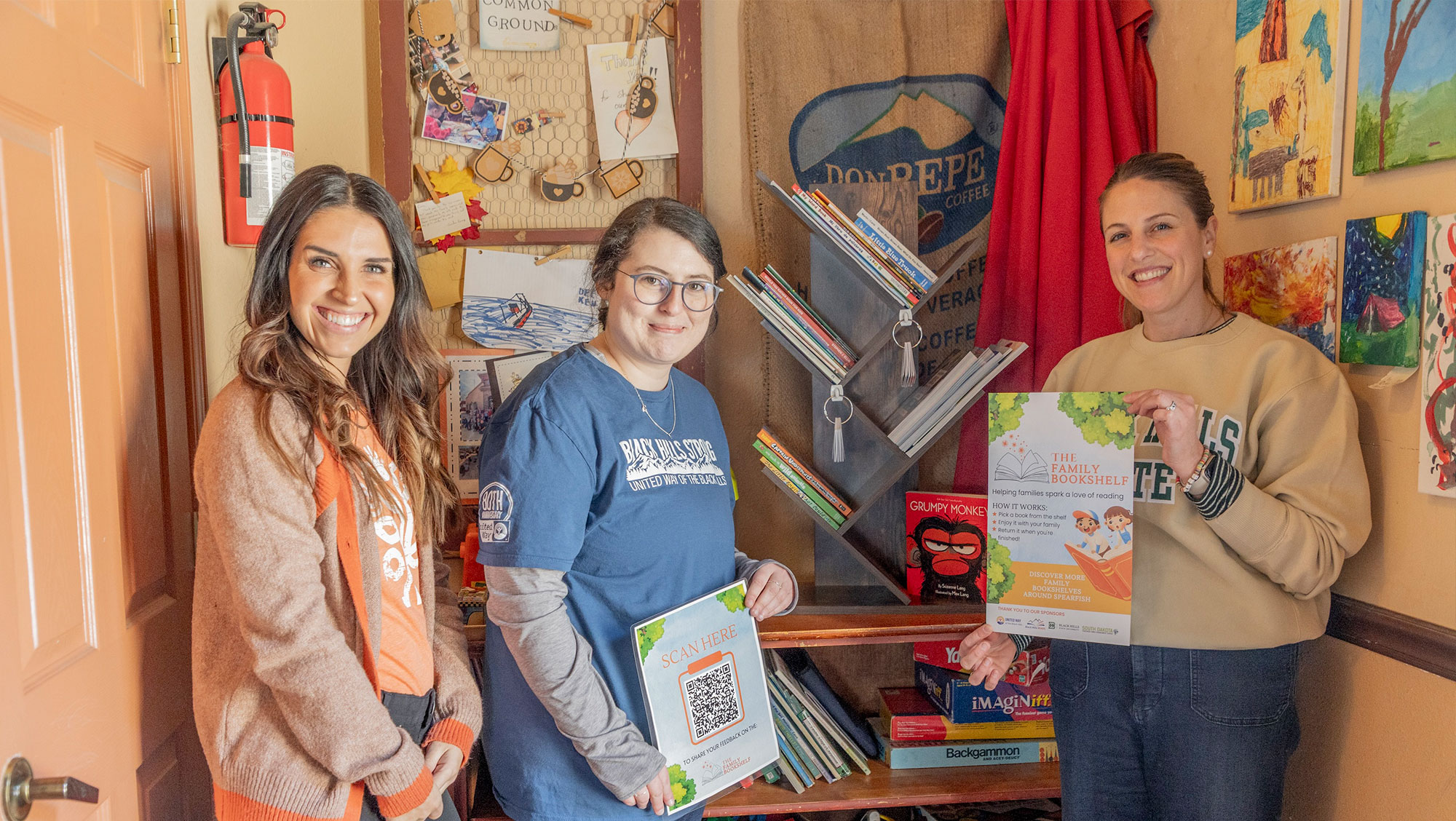 Sponsors of the Family Bookshelf Project, Maria Kemp from the South Dakota Statewide Family Engagement Center (left) and Hannah Glissendorf from United Way of the Black Hills (middle), stand alongside BHSU Professor Dr. Sydney Haugland (right) next to the newly installed community library at Common Grounds in Spearfish.