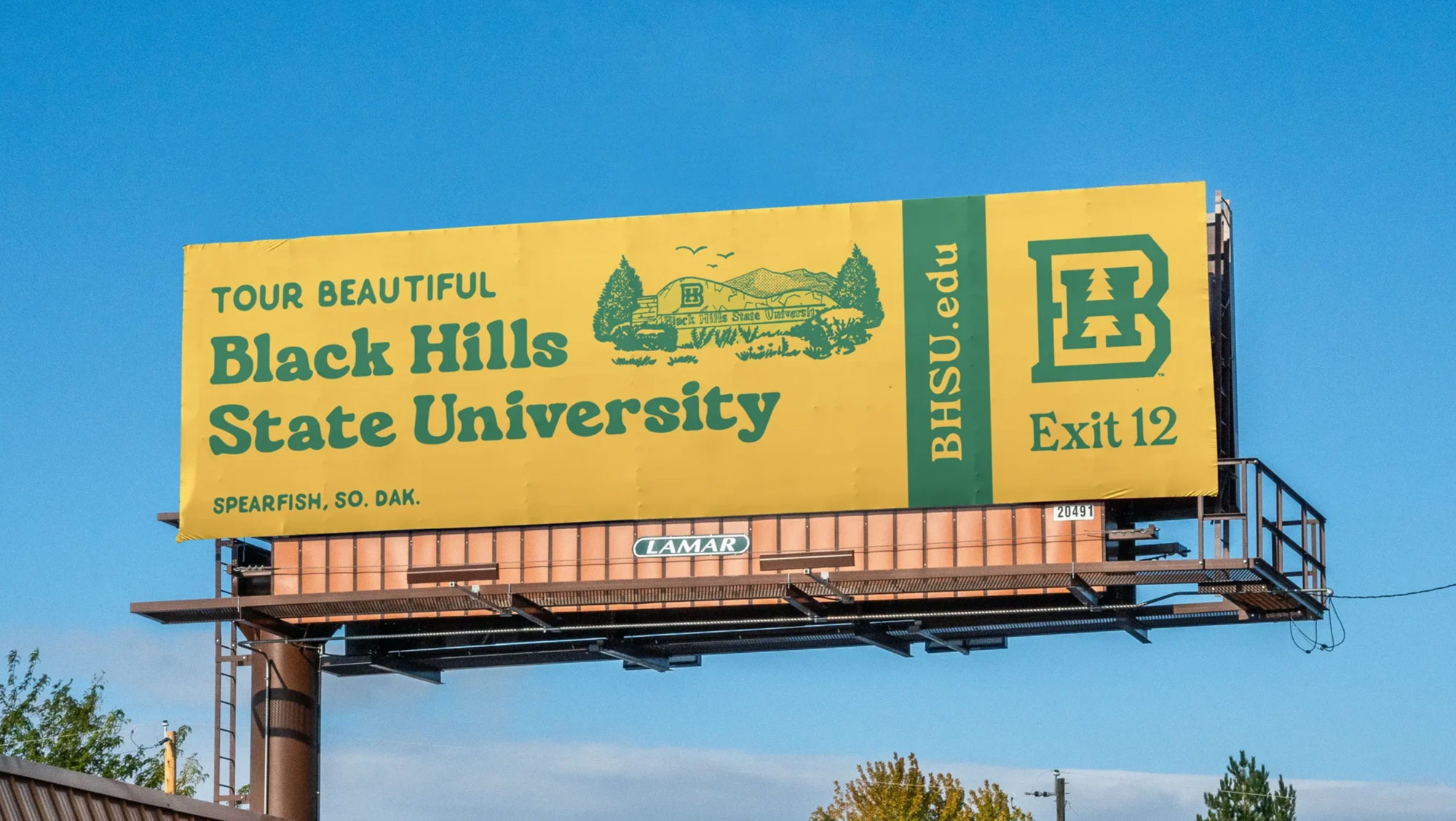 Image of a BHSU billboard. It is bright yellow with green text that says "Tour Beautiful Black Hills State University, Spearfish, So. Dak., BHSU.edu"
