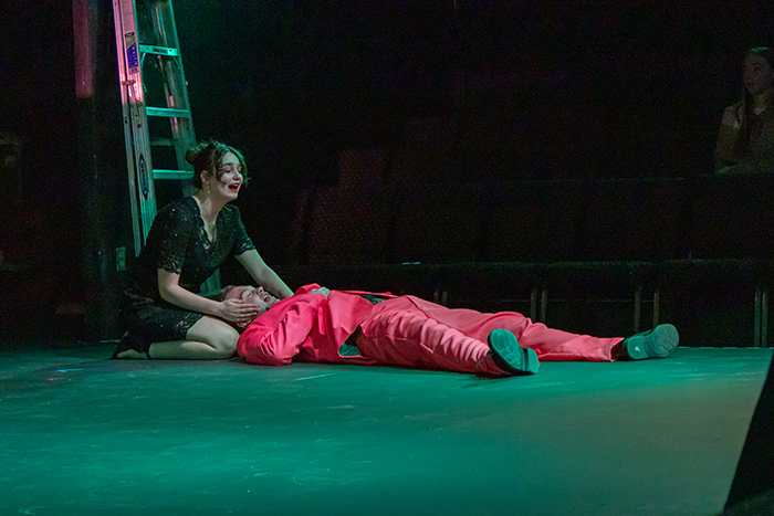 man in a pink suit laying on the ground with his head in the lap of a woman in a black dress