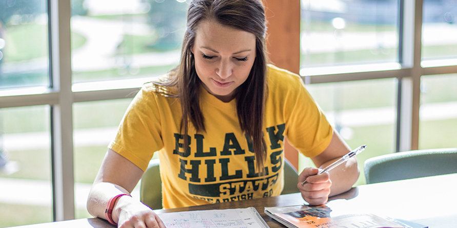 Woman sits at a table and writes in a notebook.