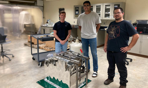 Three men standing next to a High Purity Germanium (HPGe) detector, SOLO.