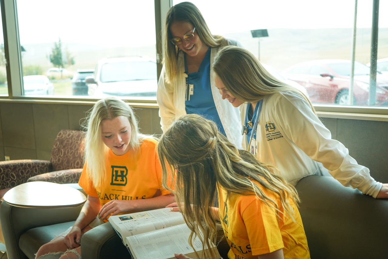 Four female nursing students studying together and reading a book.