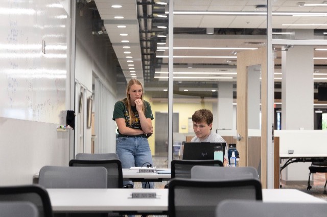 A Math Center tutor and a student engaged in a discussion around a table with books and laptops in the Math Center.