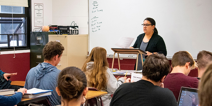 A teacher lectures a group students in a classroom.