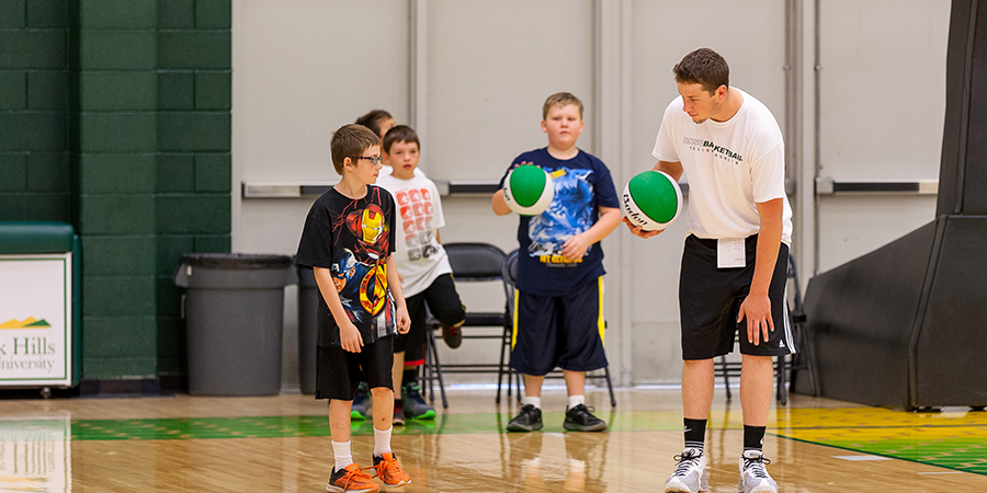 A physical education teacher shows three students how to dribble a basketball.