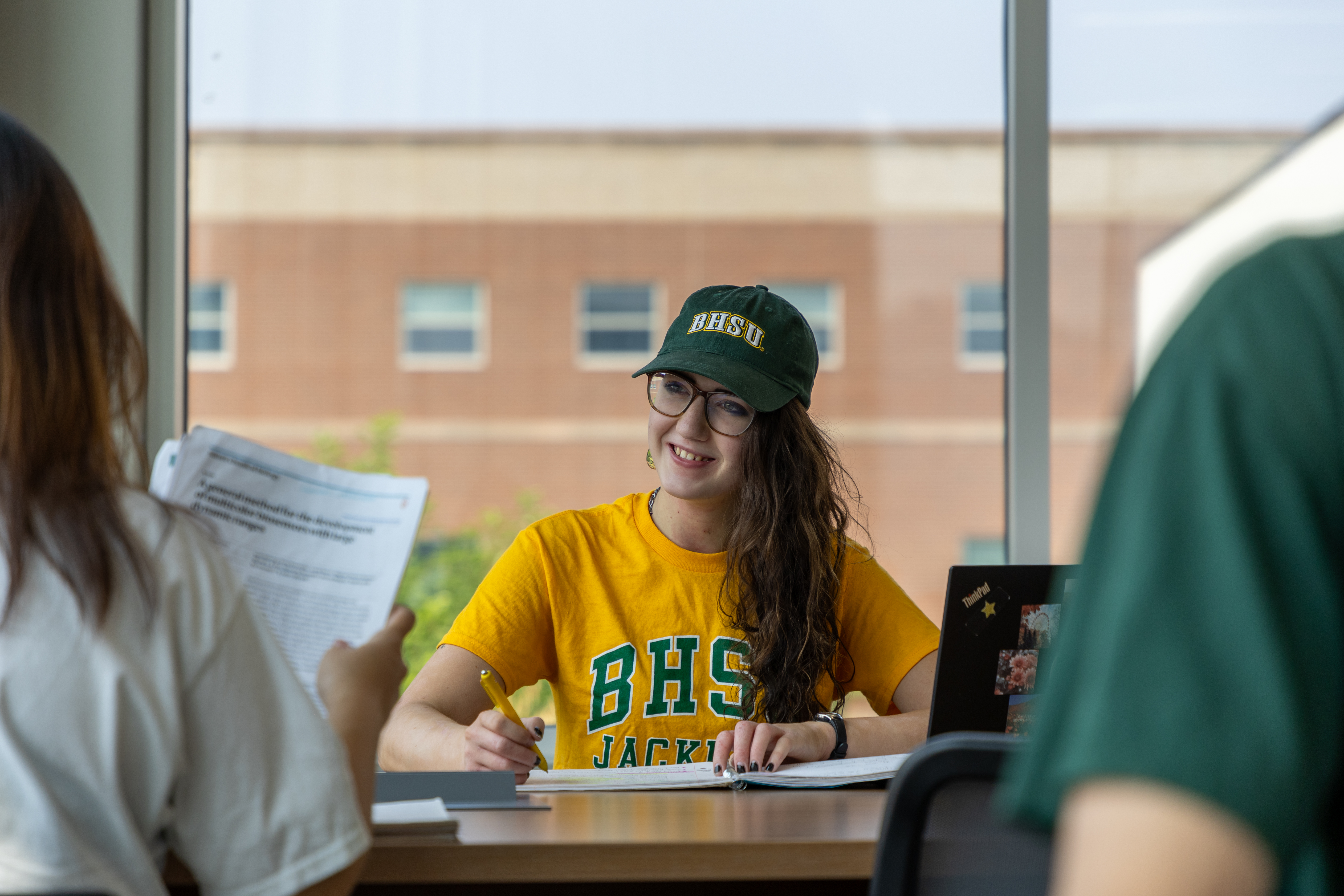 A BHSU student sits in the library with two other students sitting across from her.