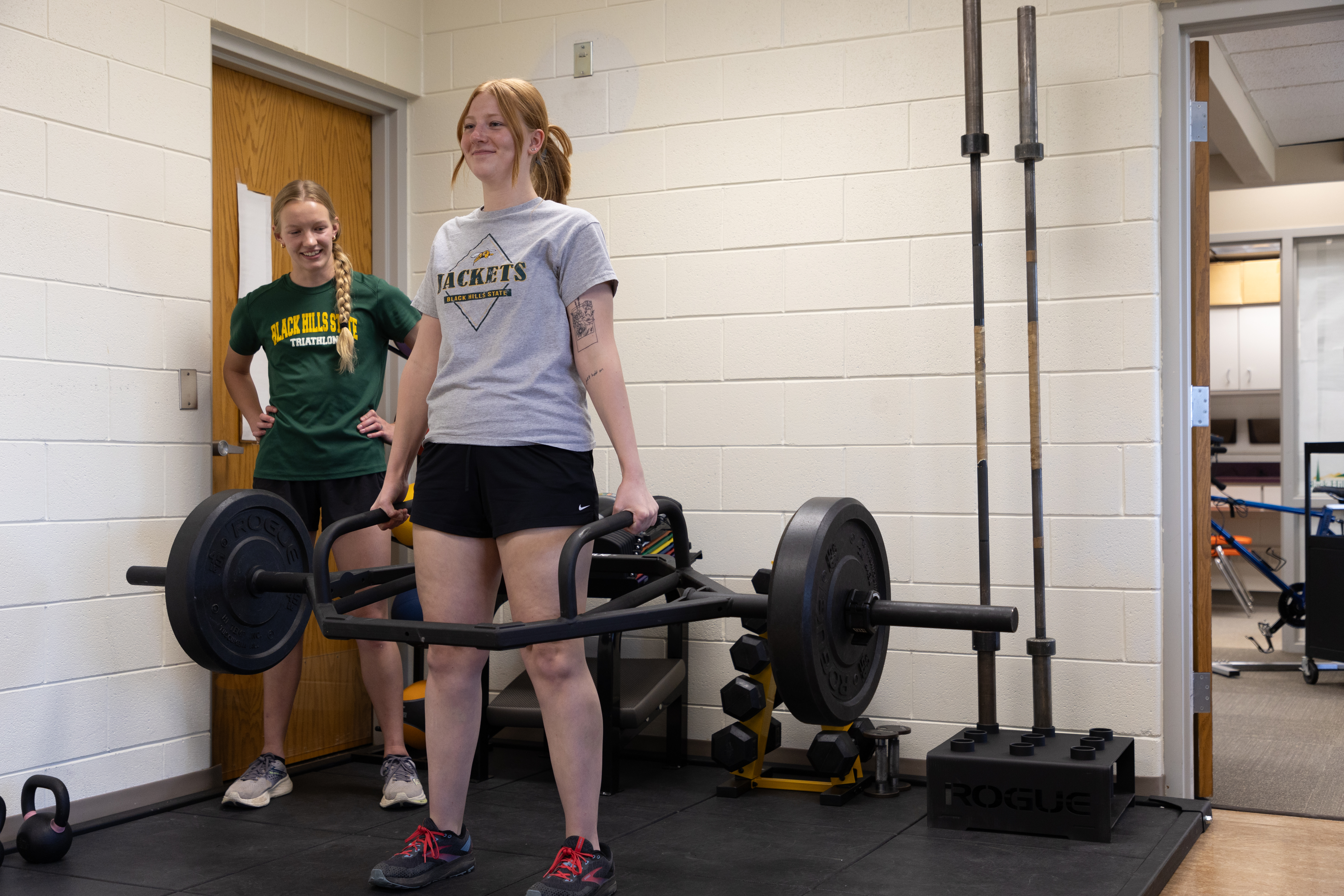 One exercise science student lifts a deadweight bar while another watches.