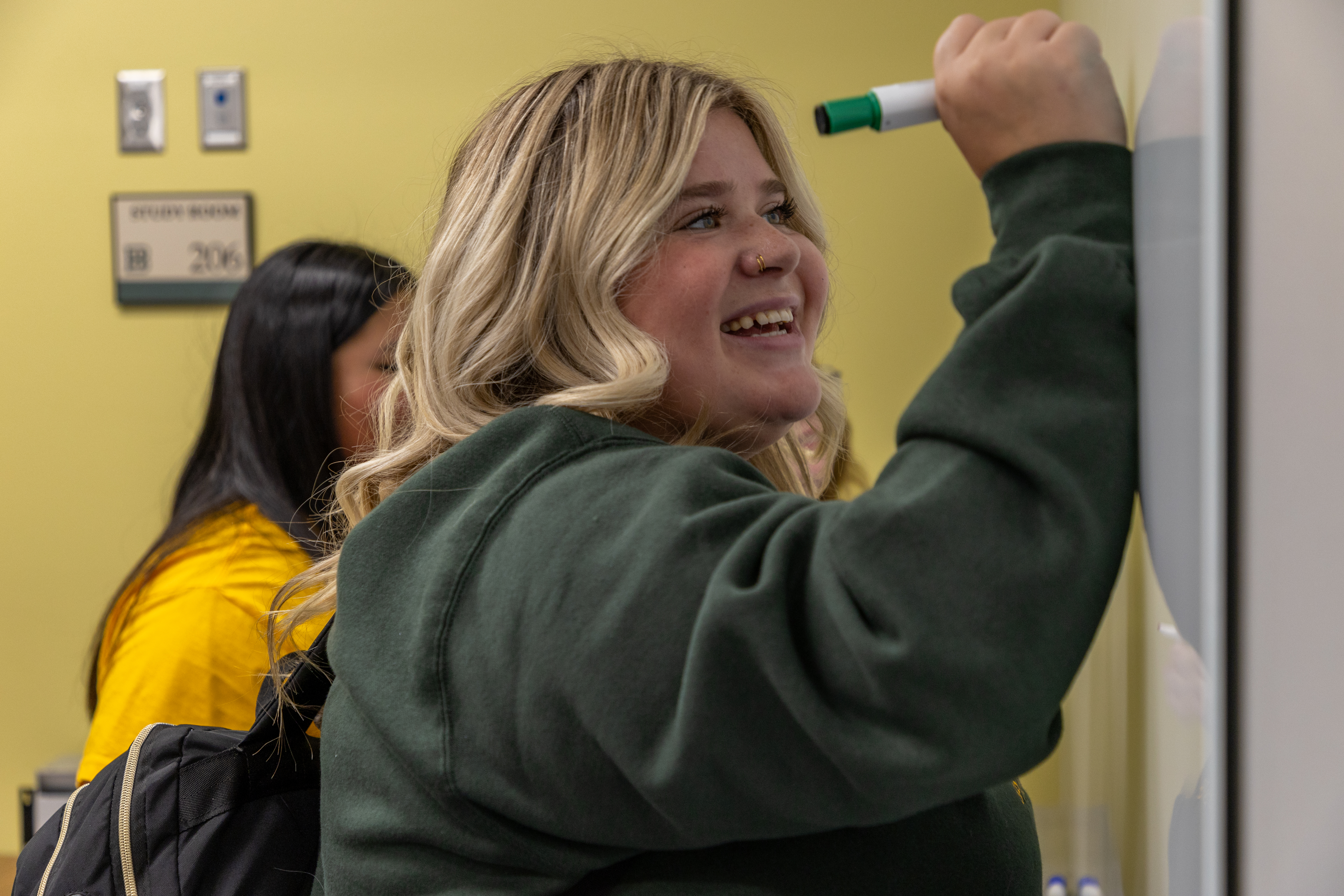 A female BHSU students takes notes on a whiteboard in a study room in the library.