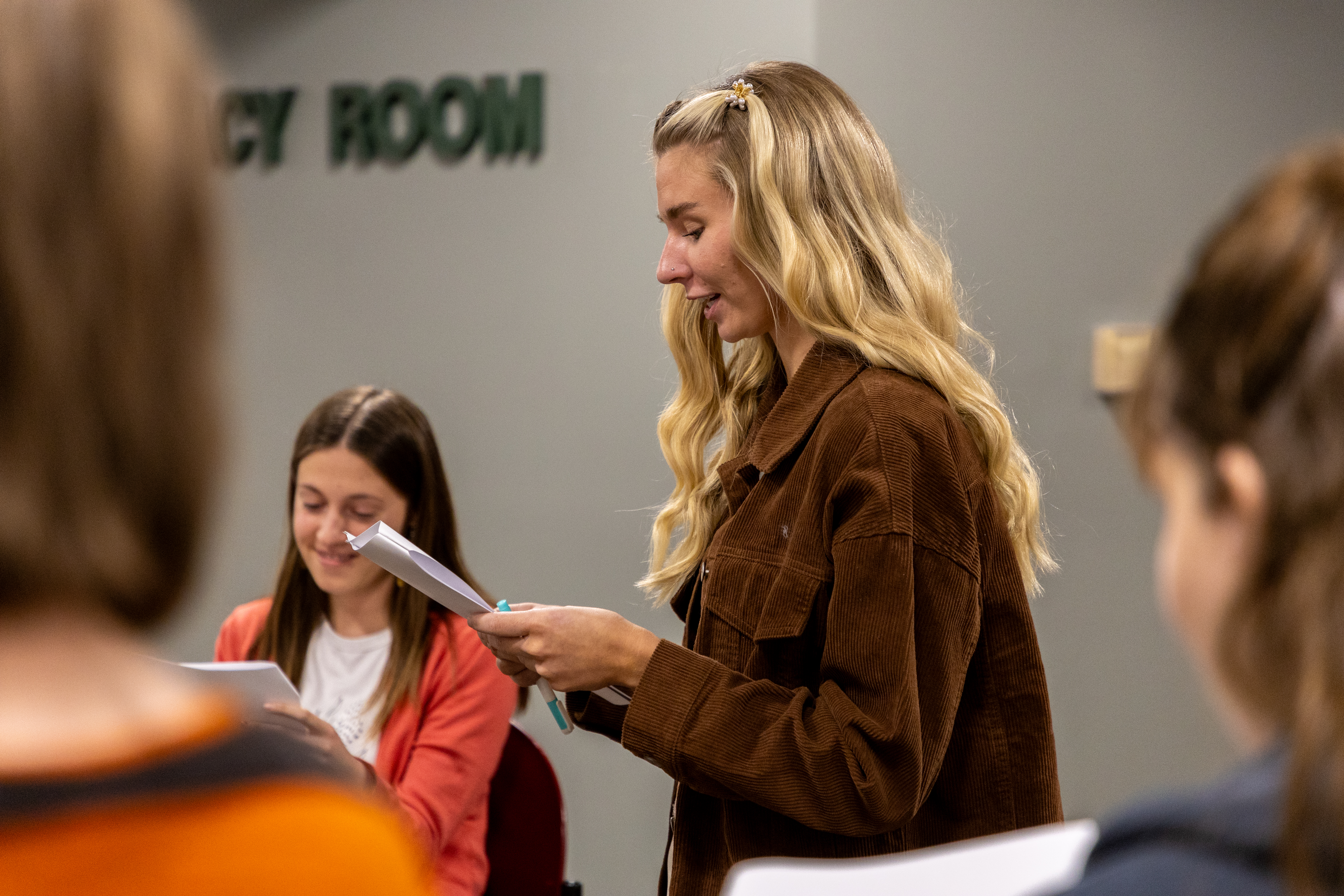 A female BHSU students stands profile to the camera reading off of a sheet of paper.