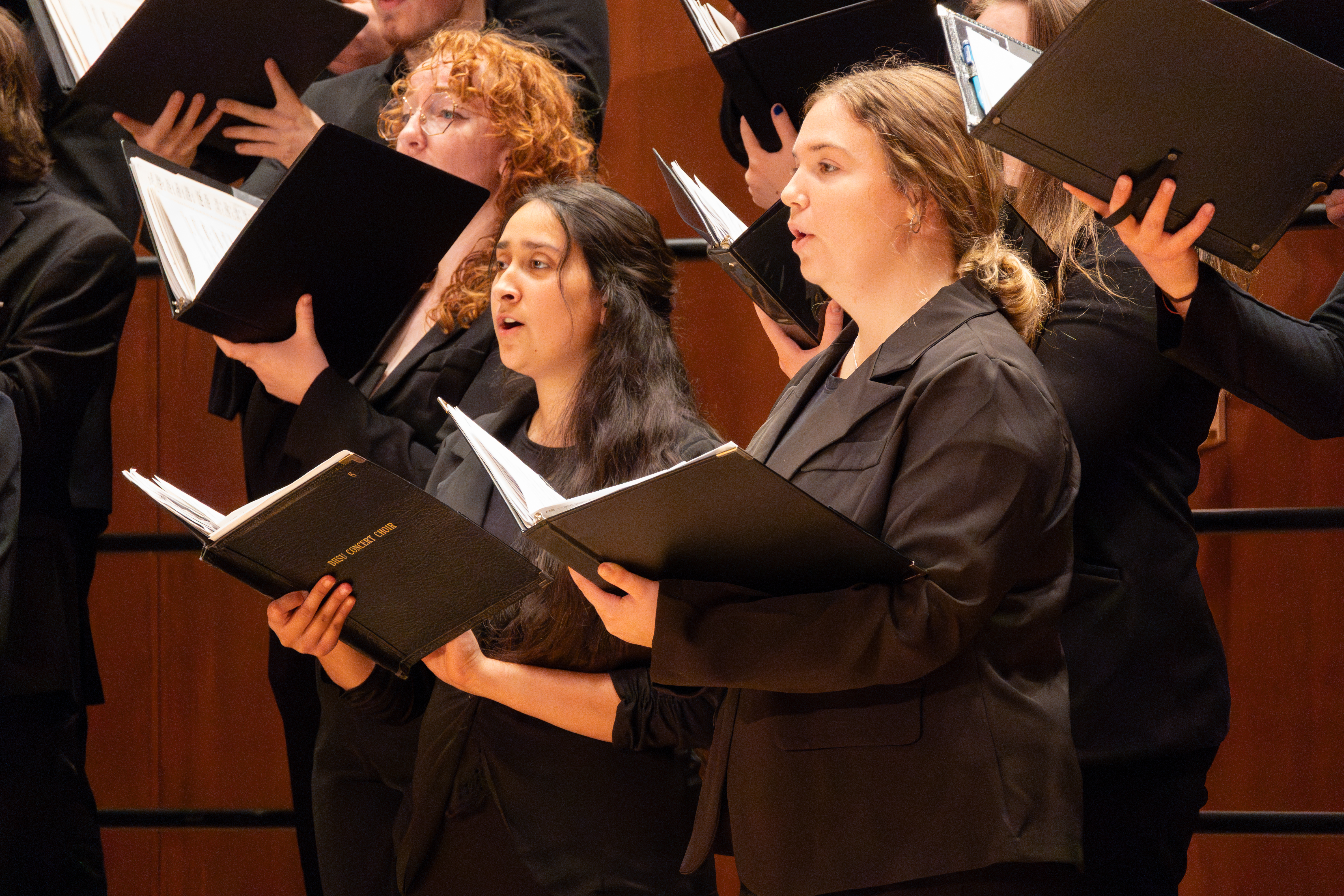 Two female students stand together singing at a choir concert.