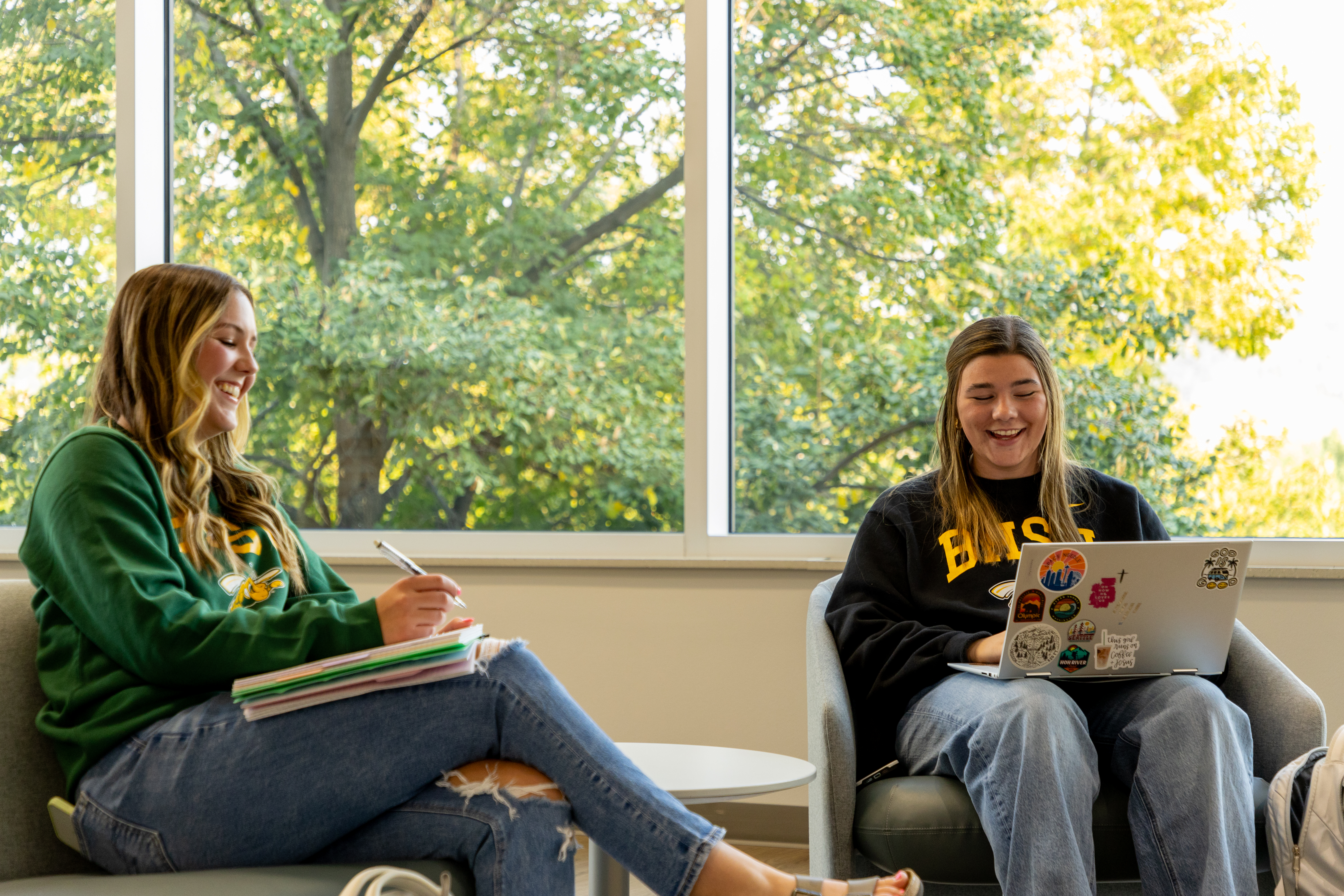 Two female BHSU sit together, one on the left taking notes and the other on the right typing on a laptop.