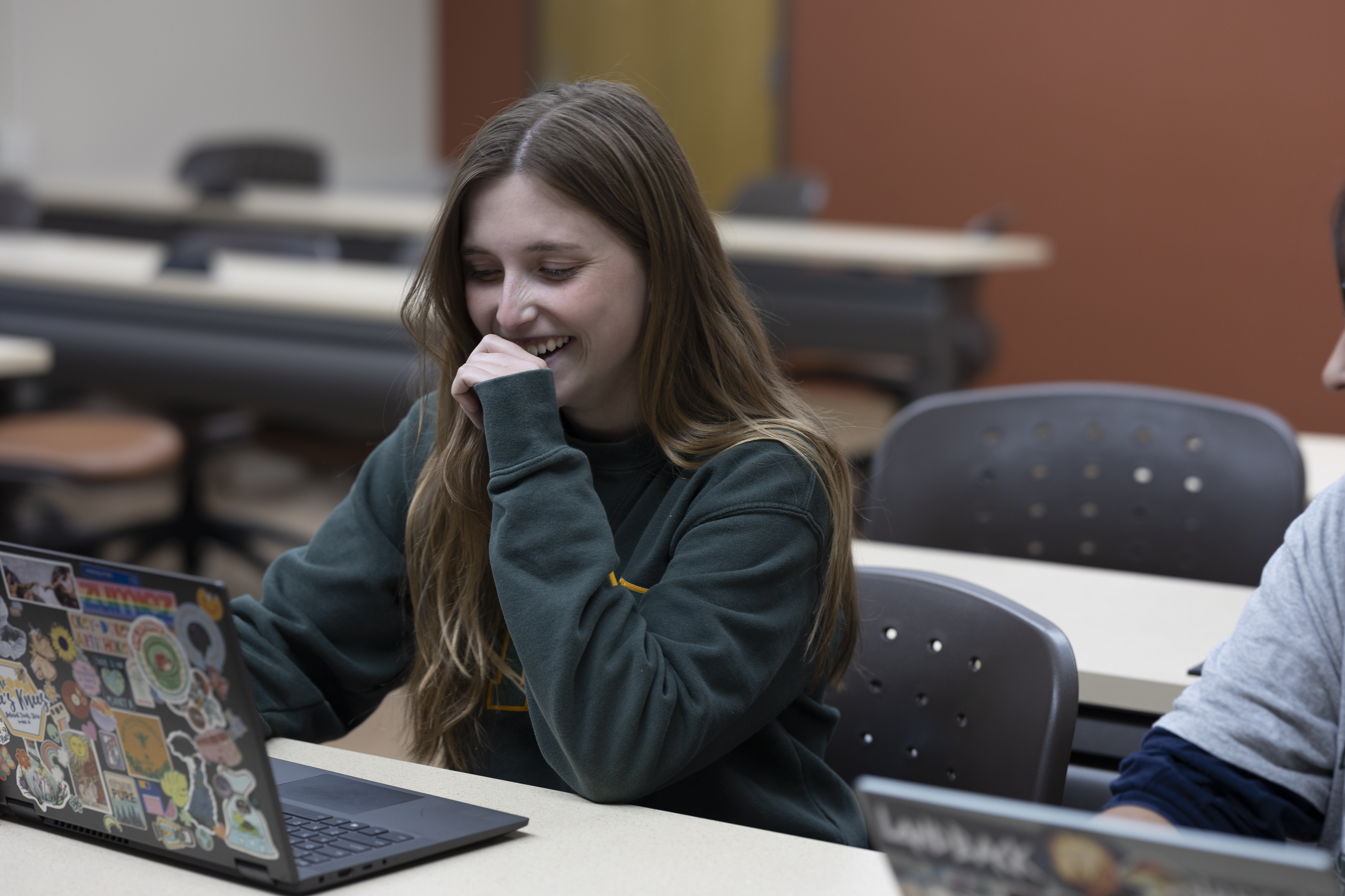 A female BHSU student laughs and types on her laptop in class.