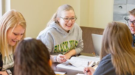 Five students sit and smile at a table together.