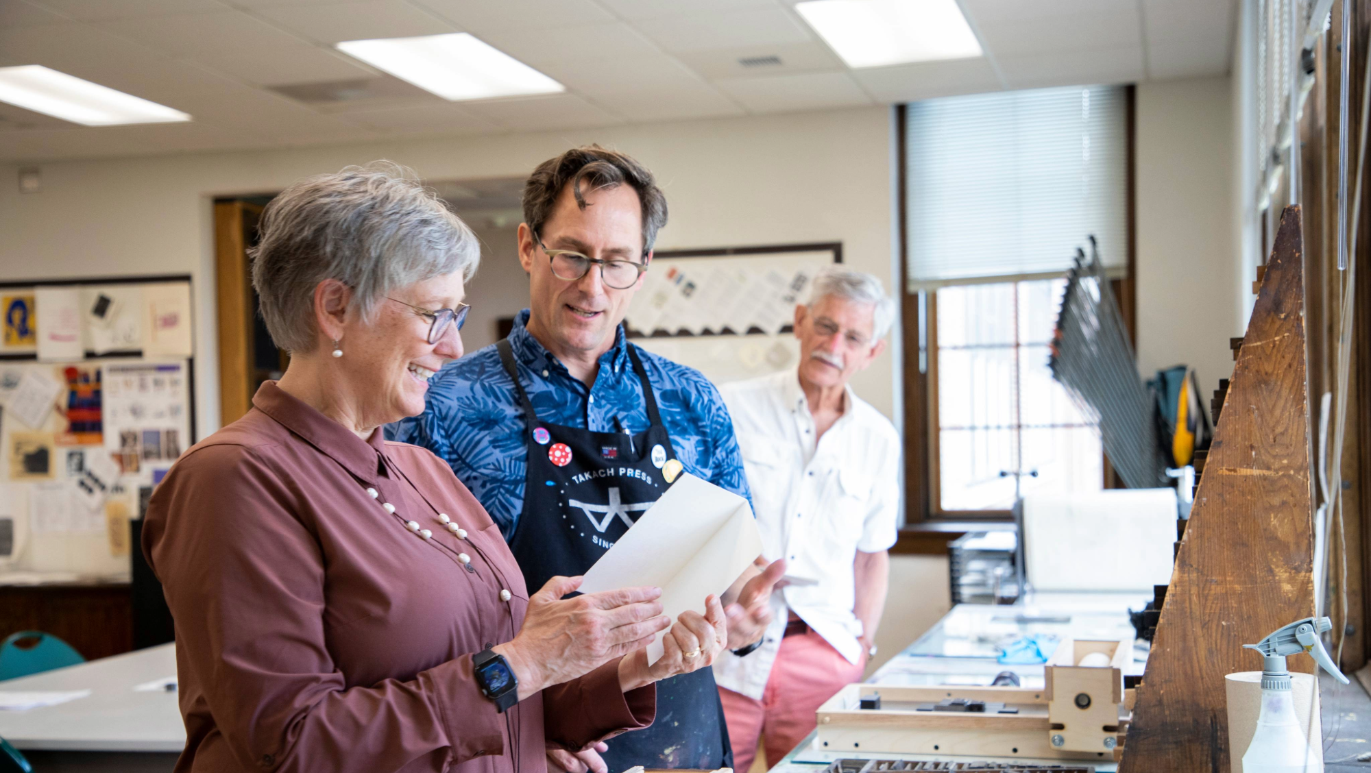 Two BHSU professors examine an object together in a printmaking studio, while another man looks on in the background.
