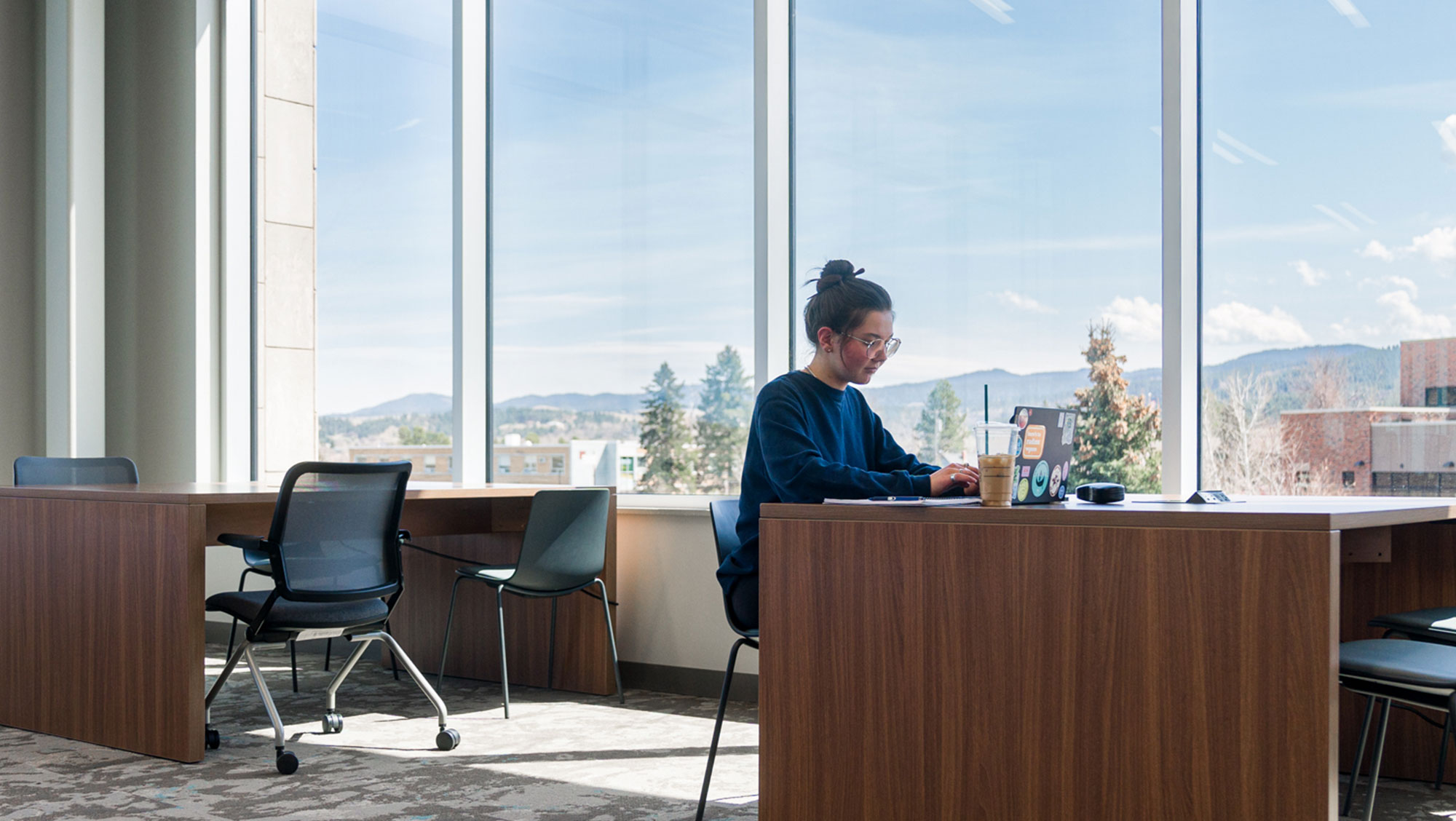 A BHSU student sits in the library with sunlight streaming in through the windows