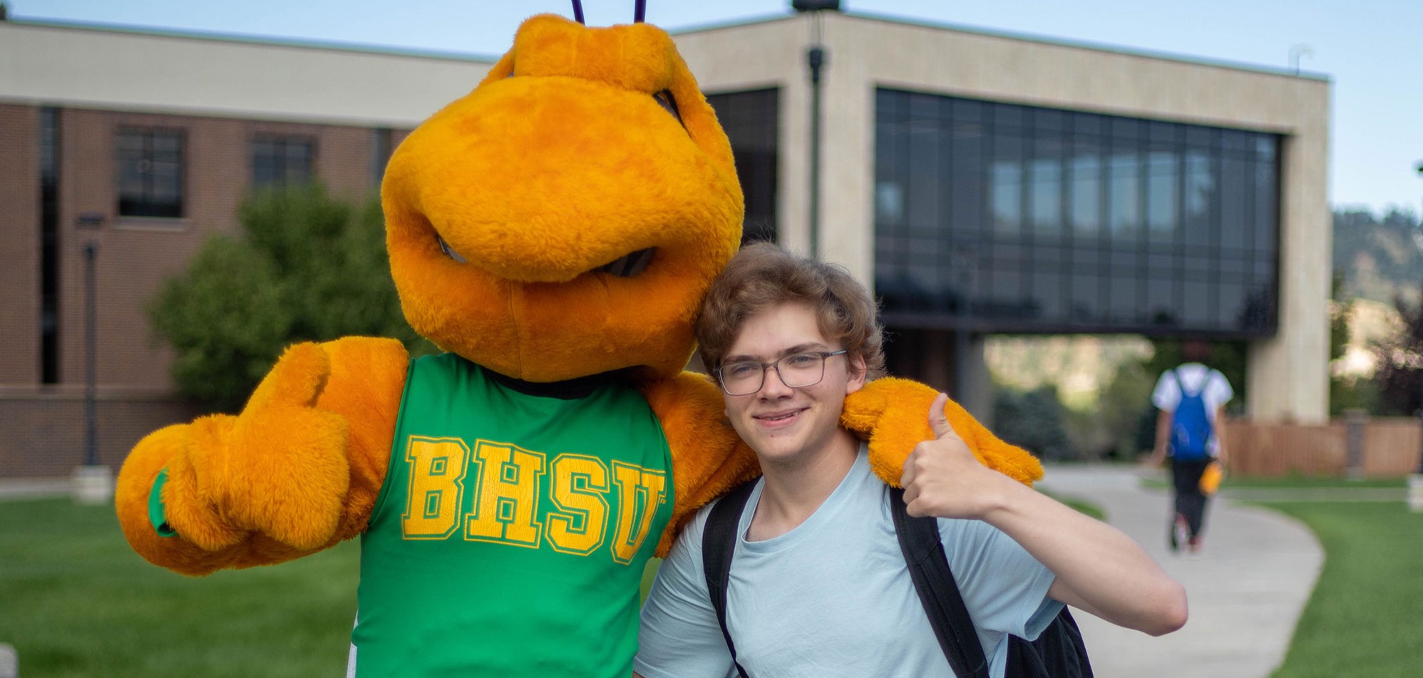 Image of BHSU mascot Sting with a student on the BHSU campus. The library building can be seen in the background.