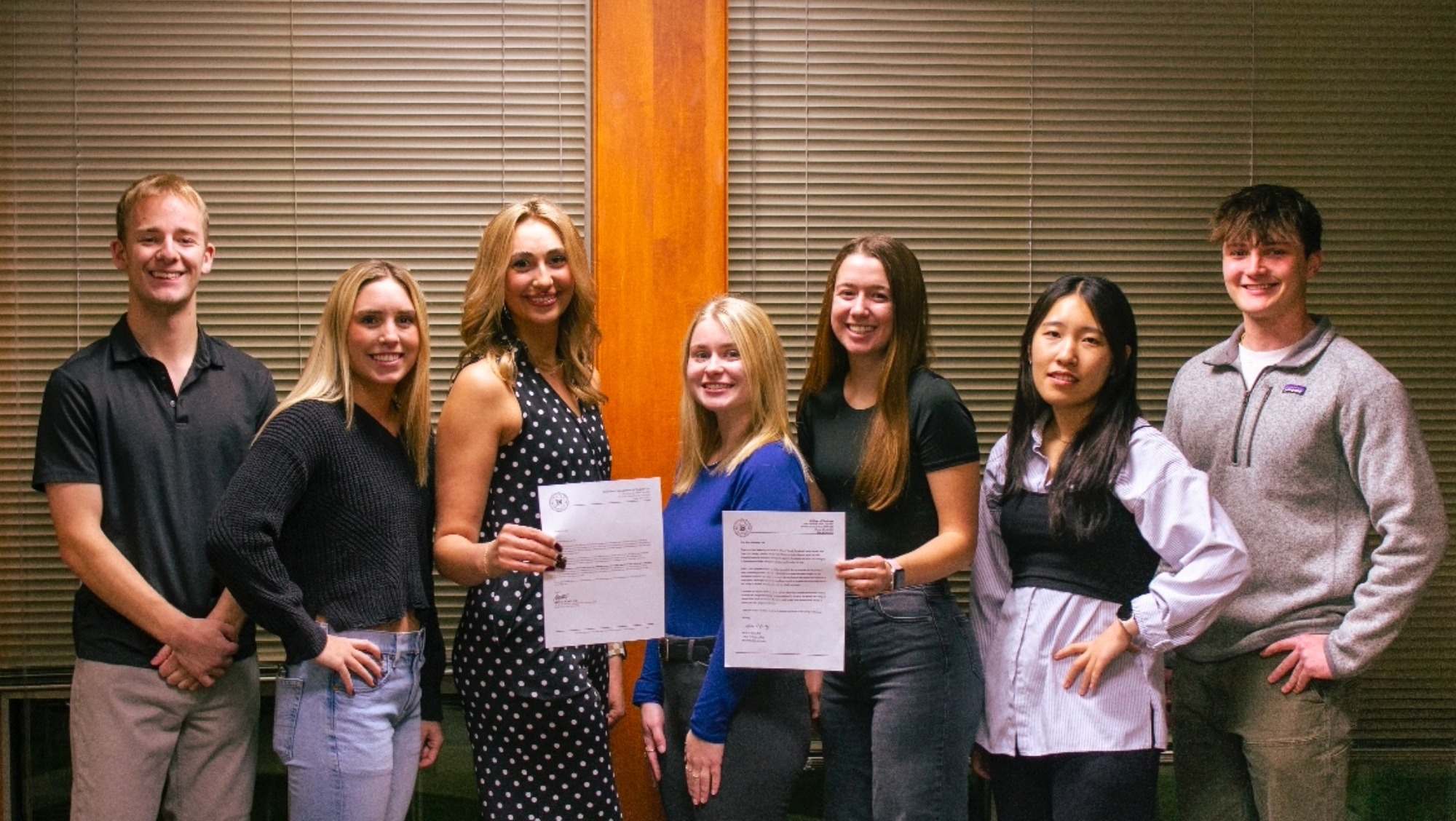 A group of seven people smile and hold two letters or recognition