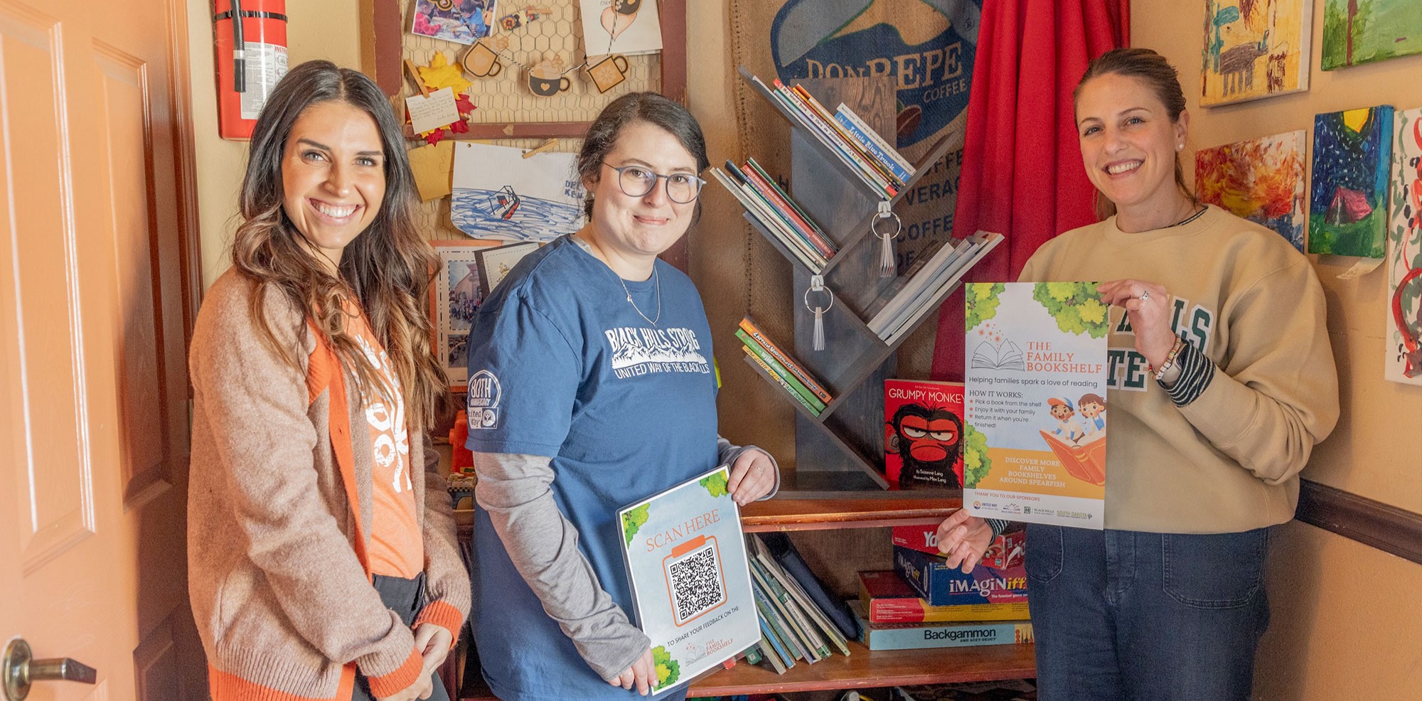 Sponsors of the Family Bookshelf Project, Maria Kemp from the South Dakota Statewide Family Engagement Center (left) and Hannah Glissendorf from United Way of the Black Hills (middle), stand alongside BHSU Professor Dr. Sydney Haugland (right) next to the newly installed community library at Common Grounds in Spearfish.